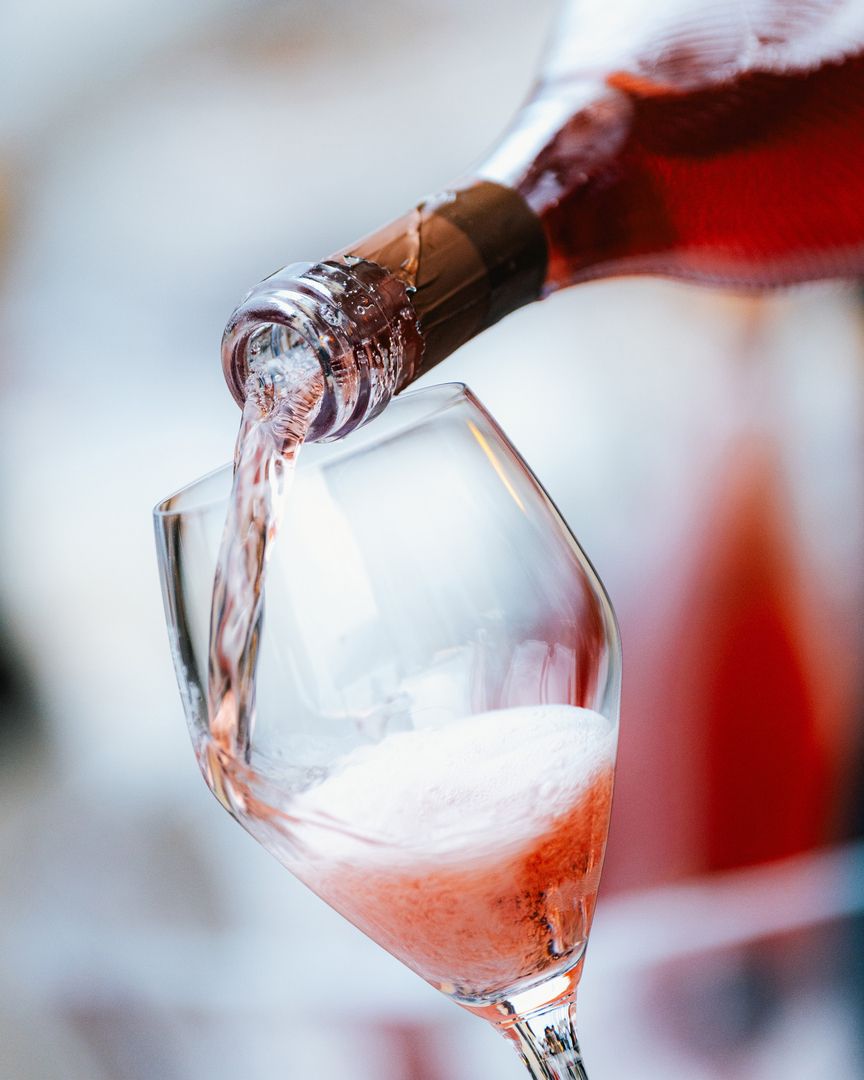 Einschenken von perlendem Rosé-Schaumwein aus einer Flasche in ein feines Glas